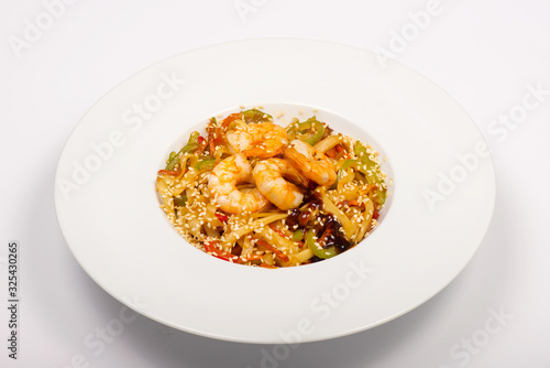 Asian style wheat noodles with shrimp, sweet peppers, sesame seeds and soy sauce in a white plate on a white background