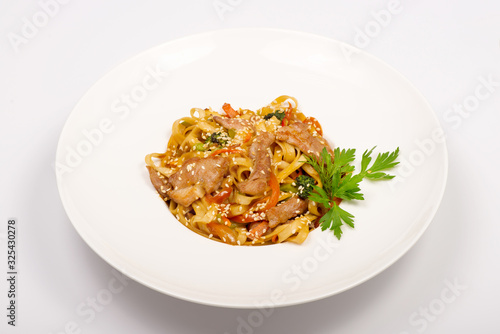 fetuccine pasta with fried chicken, red sweet pepper and sesame seeds in a white plate on a white background