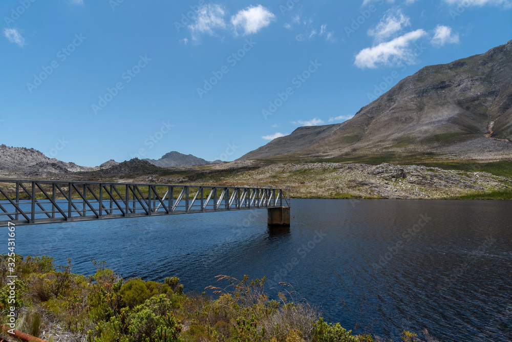 Buffels River, Western Cape, South Africa. Dec 2019. Buffels River Dam, metal walkway across the reservoir and the Hottentots Holland mountains background near Rooiels, Western Cape.