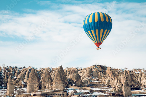 Hot air balloon flying over the fairy chimneys with snow of Cappadocia