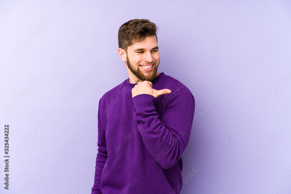 Young caucasian man isolated on purple background points with thumb finger away, laughing and carefree. Young caucasian man isolated on purple background points with thumb finger away, laughing and carefree.