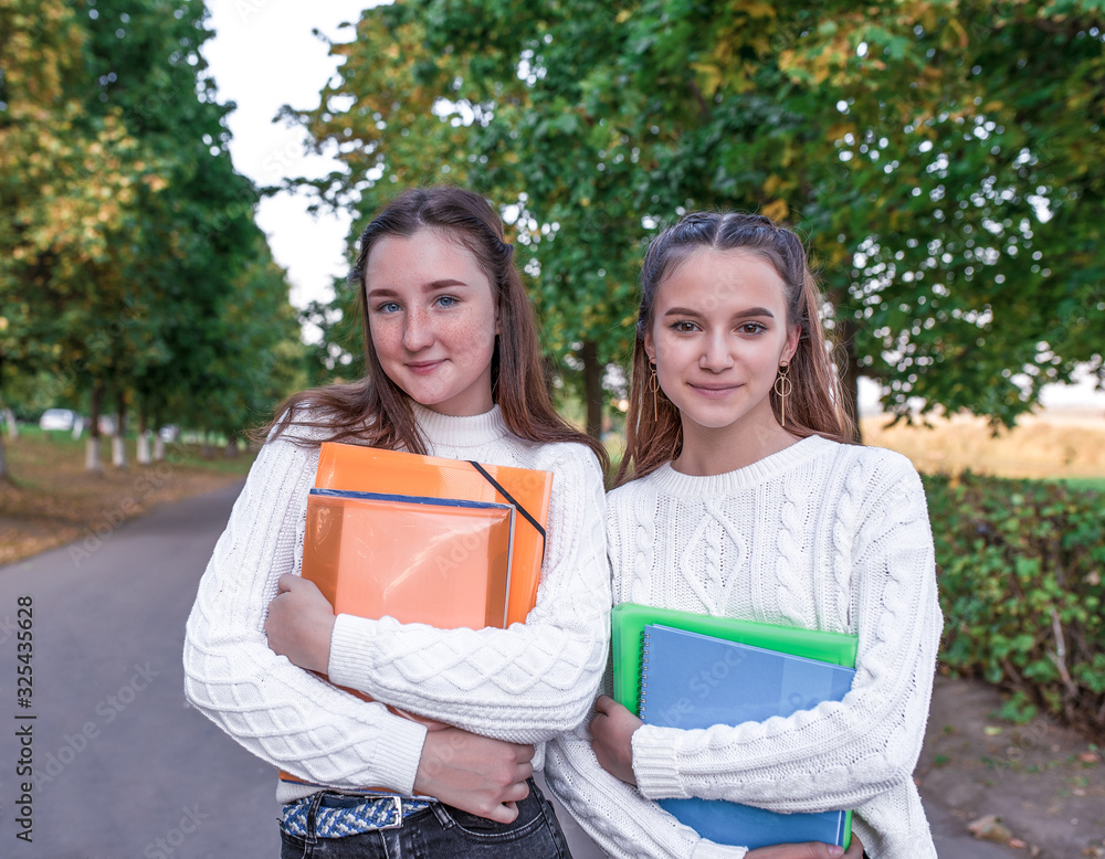 © byswat - Two girlfriends girls schoolgirls, in summer in park, happy smiles rejoice, in folders folder notebooks and notes with textbooks. Rest on a break school and college. Warm knitted sweaters. © byswat - Two girlfriends girls schoolgirls, in summer in park, happy smiles rejoice, in folders folder notebooks and notes with textbooks. Rest on a break school and college. Warm knitted sweaters.