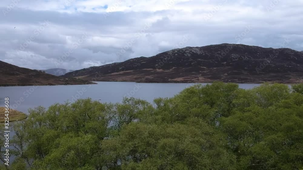 Revealing drone shot of scottish highland lake with cloudy sky and trees in foreground Revealing drone shot of scottish highland lake with cloudy sky and trees in foreground