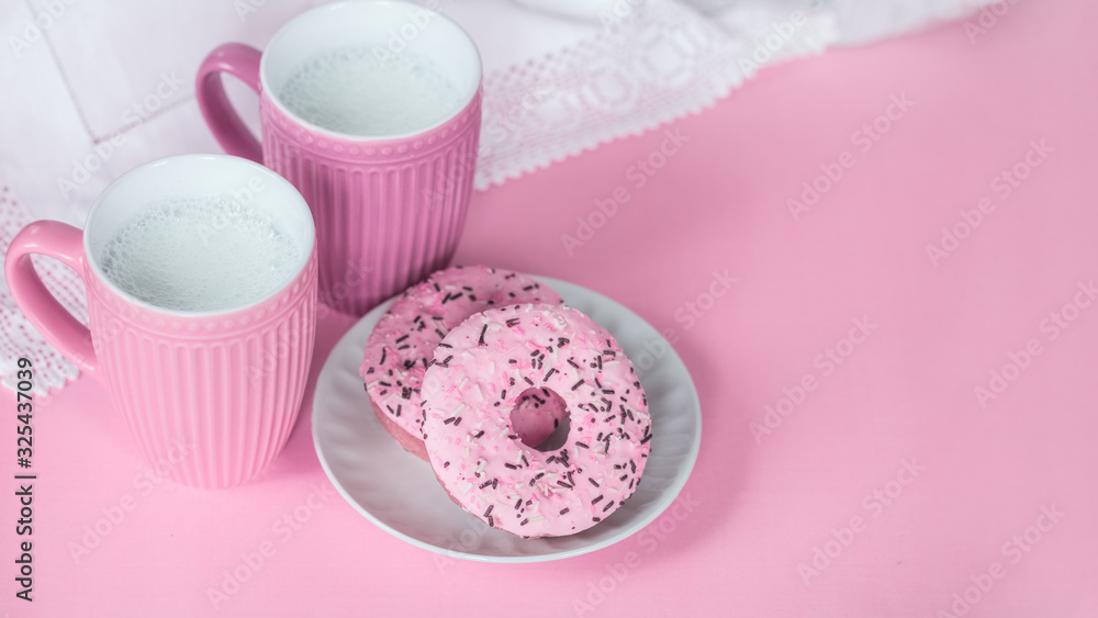 pink milk cups and doughnuts with pink frosting in a plate on a pink background top view. the milk in the cups and the cakes lay flat. milk ceramic cups and copy space. pink milk cups and doughnuts with pink frosting in a plate on a pink background top view. the milk in the cups and the cakes lay flat. milk ceramic cups and copy space.