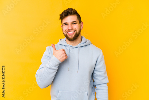Young caucasian man isolated on yellow background smiling and raising thumb up