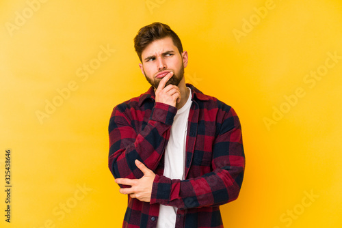 Young caucasian man isolated on yellow background looking sideways with doubtful and skeptical expression.