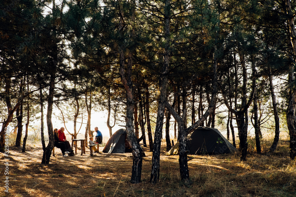 Happy family time outdoors, tourist tents, car in campsite, sunset forest picnic. Camping place on nature. Adventure travel active lifestyle. Group of people enjoy leisure holiday with sunlight rays.