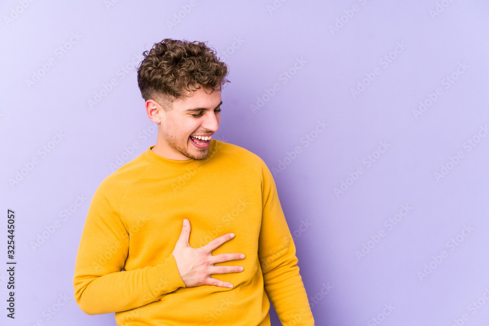 Young blond curly hair caucasian man isolated laughs happily and has fun keeping hands on stomach. Young blond curly hair caucasian man isolated laughs happily and has fun keeping hands on stomach.