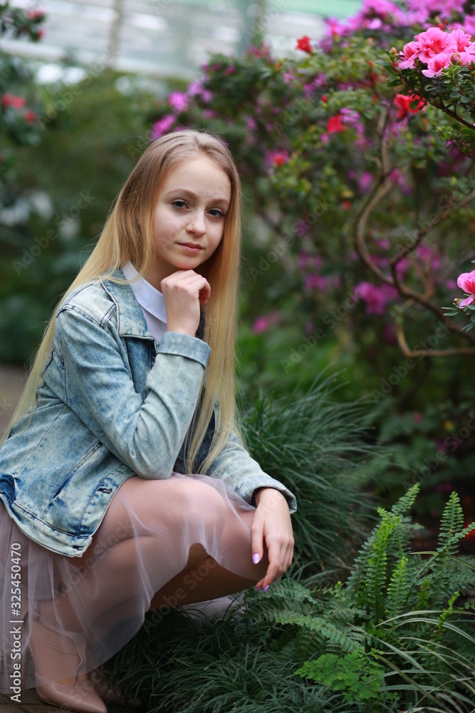 Young girl with long white hair in a denim jacket walks in the garden with blooming azalea Young girl with long white hair in a denim jacket walks in the garden with blooming azalea