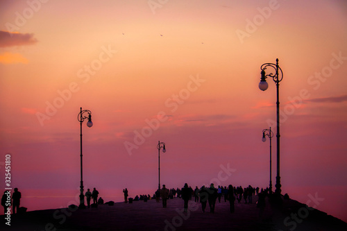 Trieste, Italy sunset promenade on the Molo Audace (Audace pier) , walking silhouettes against the red sky and sea photo