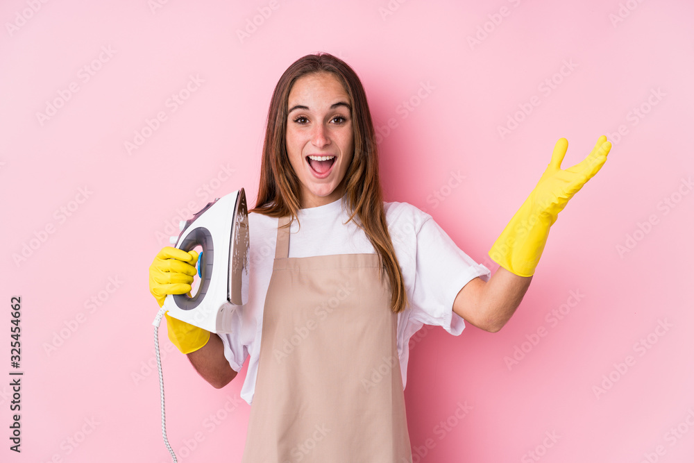 Young caucasian woman with clothes iron isolated receiving a pleasant surprise, excited and raising hands. Young caucasian woman with clothes iron isolated receiving a pleasant surprise, excited and raising hands.