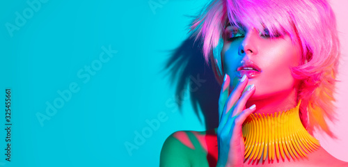Fashion model woman in colorful bright lights, portrait of beautiful party girl with trendy make-up, manicure and haircut. Art design of disco dancer, colorful make up. Over colourful vivid background