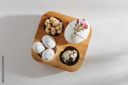 Natural Colored Eggs with flowers, easter chocolate eggs, candy and jelly bean in wooden egg box with sunlights. Stylish Compositions. Flat lay, top view