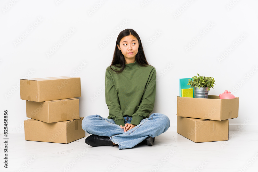 Young chinese woman moving to a new home confused, feels doubtful and unsure. Young chinese woman moving to a new home confused, feels doubtful and unsure.