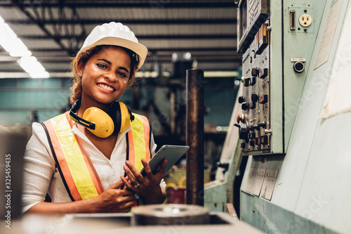 Industry maintenance engineer woman dark skin wearing uniform and safety helmet under inspection and checking production process on factory station by tablet. Industry, Engineer, construction concept. photo