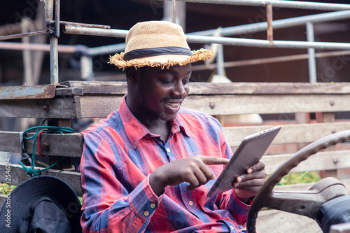African farmer man using tablet with happy and smiling on old tractor