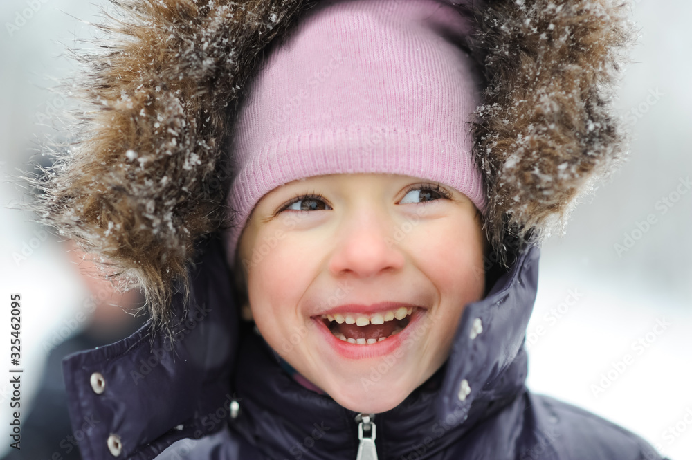 Little girl close-up portrait smiling and walking in the winter outdoors. Children outdoor. Happy kid, child having fun in beautiful winter park during snowfall. Little girl close-up portrait smiling and walking in the winter outdoors. Children outdoor. Happy kid, child having fun in beautiful winter park during snowfall.
