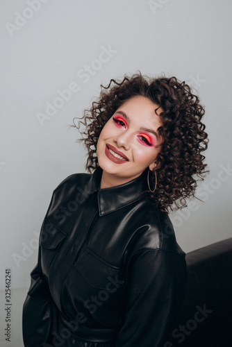 girl with bright makeup and curly hair in a black leather dress on a light background