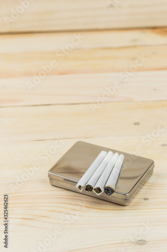 Joint of cannabis on cigarette box for smoking, on wooden background.