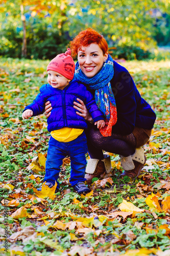 Happy mother with her son walking on nature autumn leaves in park. Family spending time together. Mom holding her kid  little baby boy  playing  having fun  smiling outdoors.