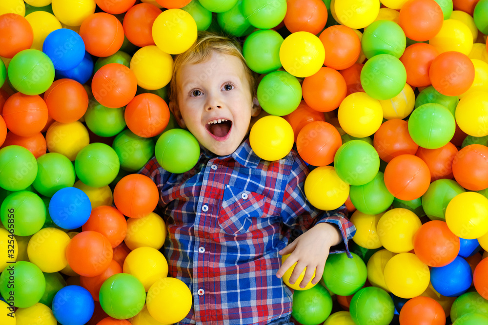 Happy child, kid boy playing, having fun on playground with colorful plastic balls in pool. Game center for family weekend, holiday party with kids, games area room. Entertainment center with toys. - obrazy, fototapety, plakaty 