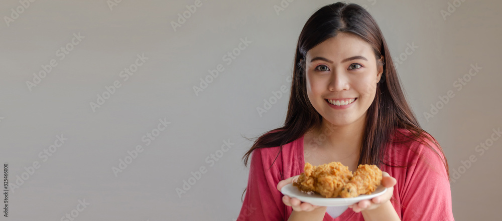Panoramic banner copy space. asian young pretty woman slim body smiling and holding delicious crispy fried chicken on dish in kitchen at home, junk food, unhealthy food, dieting, weight loss concept