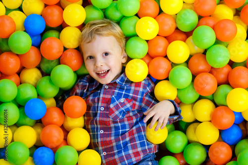 Happy child, kid boy playing, having fun on playground with colorful plastic balls in pool. Game center for family weekend, holiday party with kids, games area room. Entertainment center with toys.