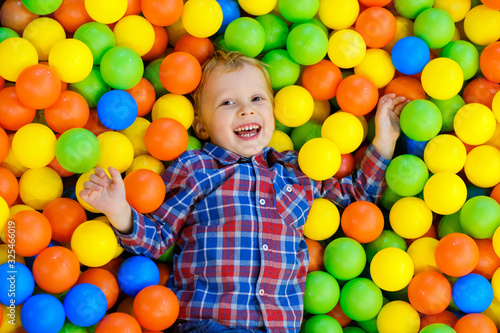 Happy child, kid boy playing, having fun on playground with colorful plastic balls in pool. Game center for family weekend, holiday party with kids, games area room. Entertainment center with toys.