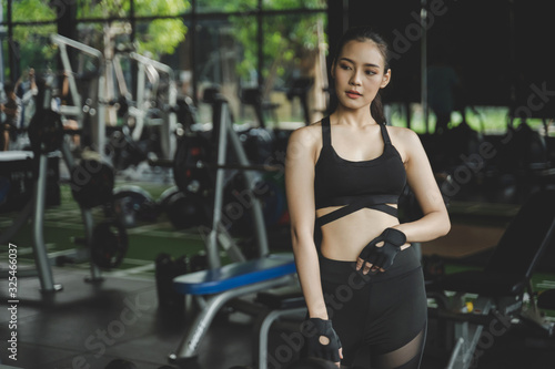 athletic young asian pretty slim body woman posing and looking her body in the mirror with machine in fitness gym, bodybuilder, healthy lifestyle, exercise fitness, workout and sport training concept