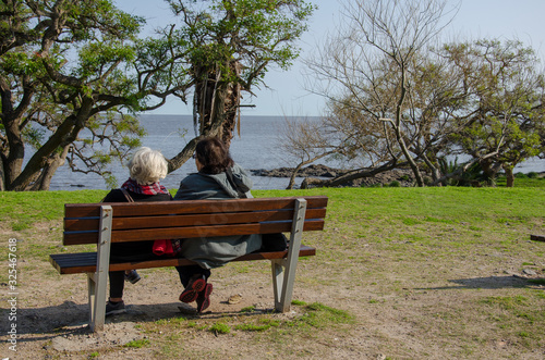two old women sitting on a park bench with lake in front