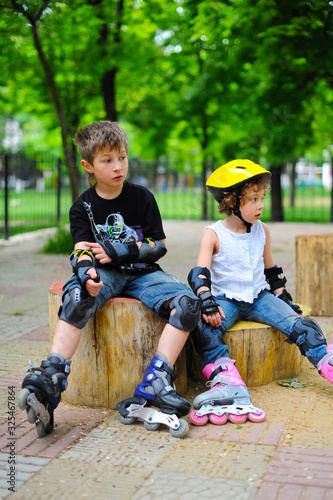 Little girl and boy, friends in roller skates in park at summer. Pretty children, kids, brother and sister riding a roller, wearing roller skates and protective equipment.