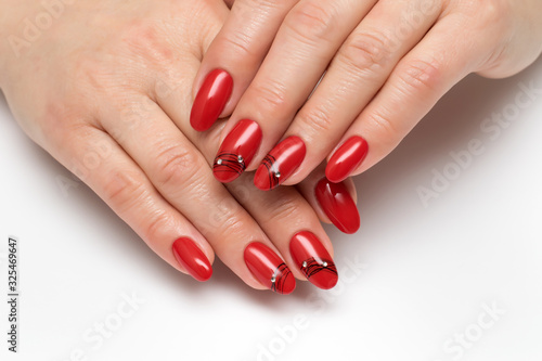 Red manicure on long oval nails with a black spider web and crystals close-up on a white background.