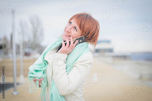 Beautiful girl in autumn weather talks on the phone  smiles and rejoices