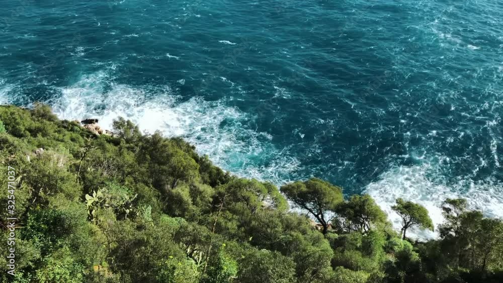 top view of sea waves hitting coastline on the beach with turquoise blue sea water. green trees on cliff seascape in Atlantic ocean. splashing water with spray and foam. top view of sea waves hitting coastline on the beach with turquoise blue sea water. green trees on cliff seascape in Atlantic ocean. splashing water with spray and foam.