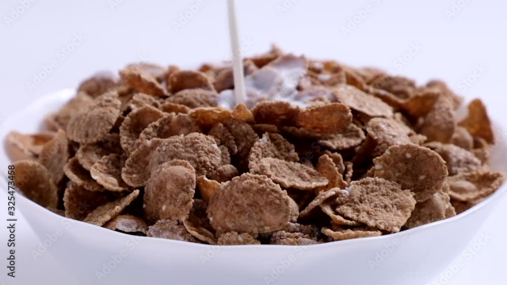 Milk is poured to bowl with natural whole grain wheat flakes. Healthy breakfast concept. Plate with multigrain flakes on white background. Slow motion Milk is poured to bowl with natural whole grain wheat flakes. Healthy breakfast concept. Plate with multigrain flakes on white background. Slow motion