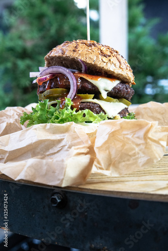 Burger na industrialnym stole w ekologicznym papierze. Duży lunch, burger meksykański grillowany na ogrodzie. Burger w bułce pełnoziarnistej.