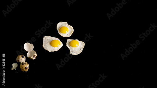 Three baked quail eggs on a black background. There are eggshells near. 