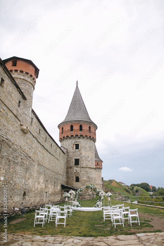 Wedding ceremony at old castle. Wedding reception and decor, round arch with flowers near ancient tower and wall of old Kamianets-Podilskyi castle, Ukraine Wedding ceremony at old castle. Wedding reception and decor, round arch with flowers near ancient tower and wall of old Kamianets-Podilskyi castle, Ukraine