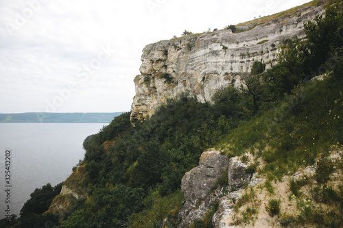 Beautiful stone cliff and big lake. Old stone caves, green hill and river landscape. Bakota lake and Dnister river in Ukraine.Travelling and exploring national park. Summer vacation