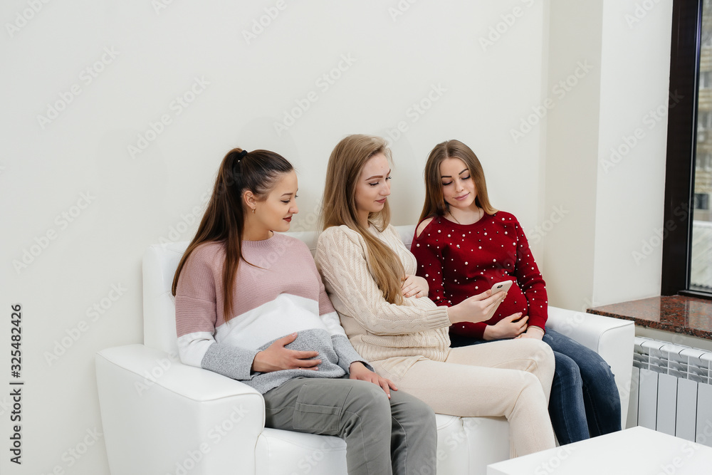 Pregnant girls sit on the couch and have fun chatting with each other. Pregnancy and taking care of the child's future