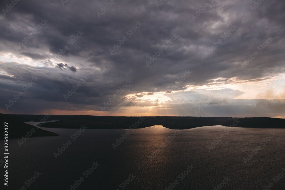 Beautiful view of sun rays from dark clouds above lake. Sunset light over hill and river landscape. Dramatic moody scenery. Bakota lake and Dniester river in Ukraine