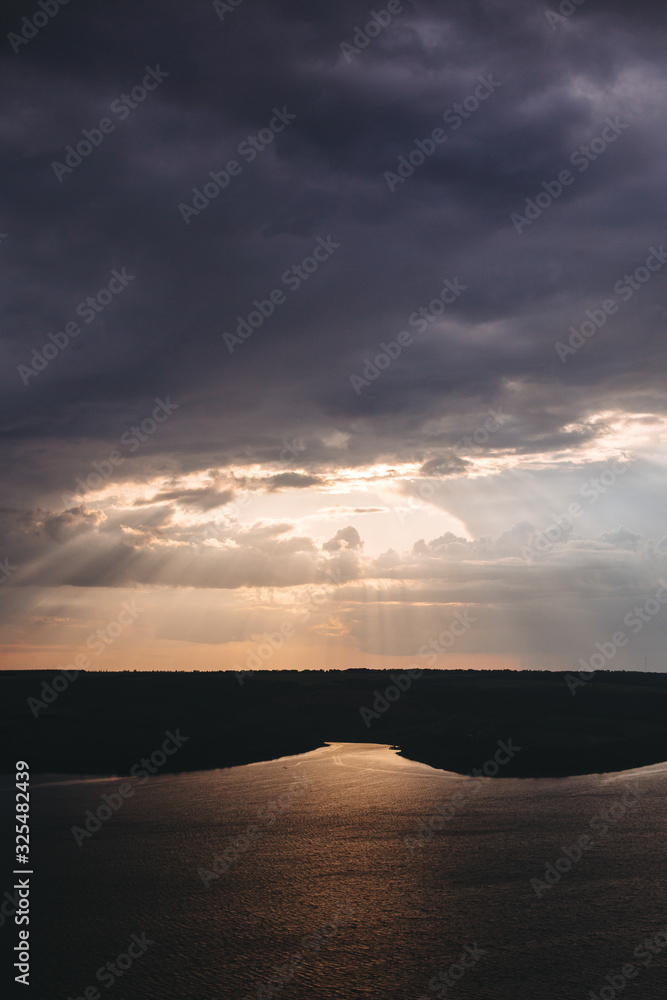 Beautiful view of sun rays from dark clouds above lake. Sunset light over hill and river landscape. Dramatic moody scenery. Bakota lake and Dniester river in Ukraine