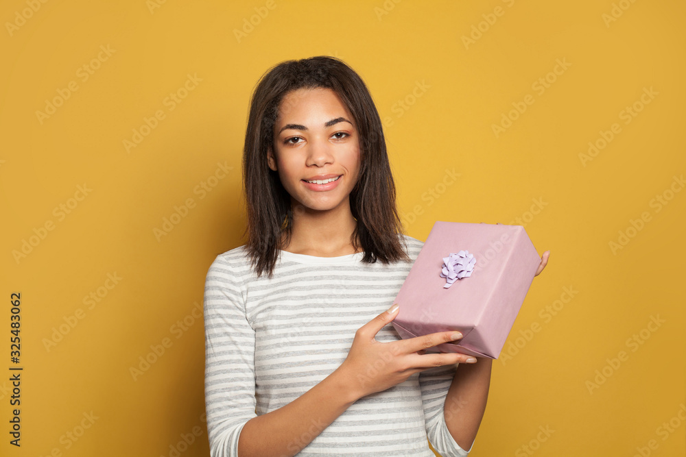 Positive african american woman with gift on bright yellow background Positive african american woman with gift on bright yellow background