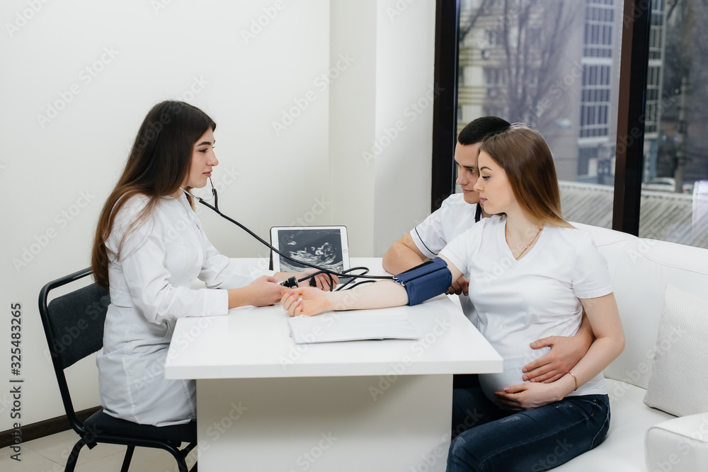The doctor measures the pressure of a pregnant girl in the clinic. Pregnancy, and health care The doctor measures the pressure of a pregnant girl in the clinic. Pregnancy, and health care