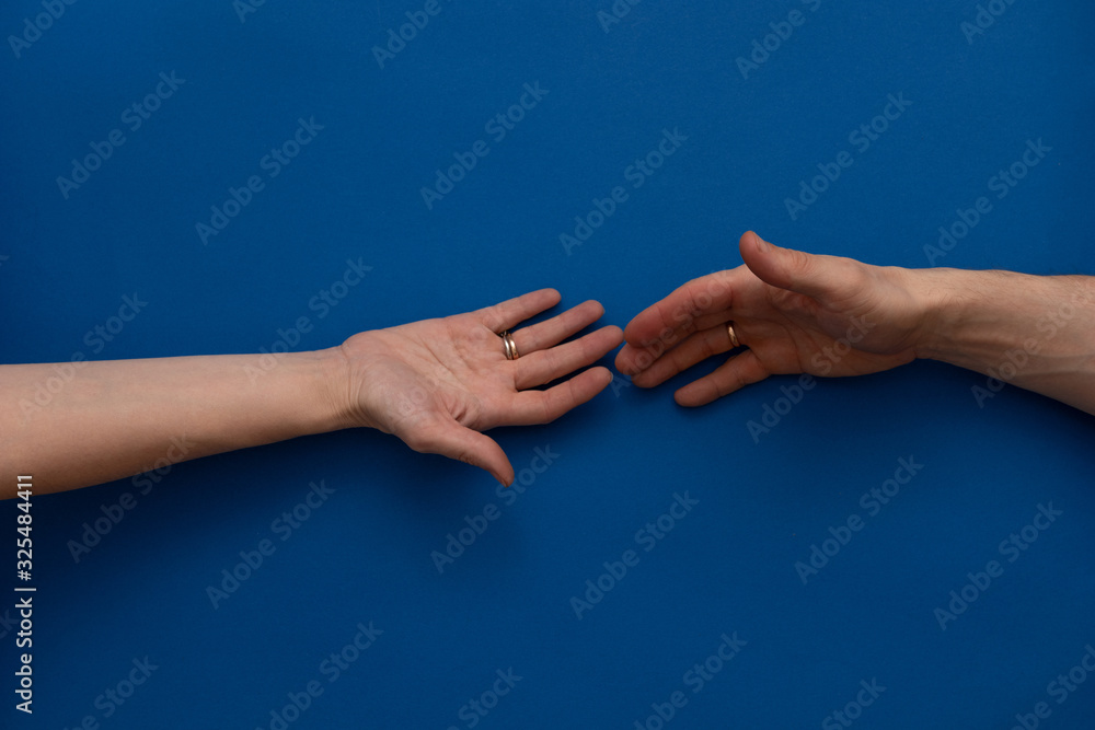 Female hand with a wedding ring reaches for a male hand with a wedding ring on a blue background. Concept support, help.