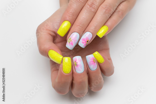 Bright yellow and blue summer manicure with painted flowers on square long nails with sparkles. Sunny manicure. Pink flowers. Close-up on a white background.
