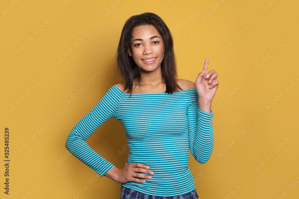 Young smiling woman fashion model pointing finger up on vivid yellow studio background Young smiling woman fashion model pointing finger up on vivid yellow studio background