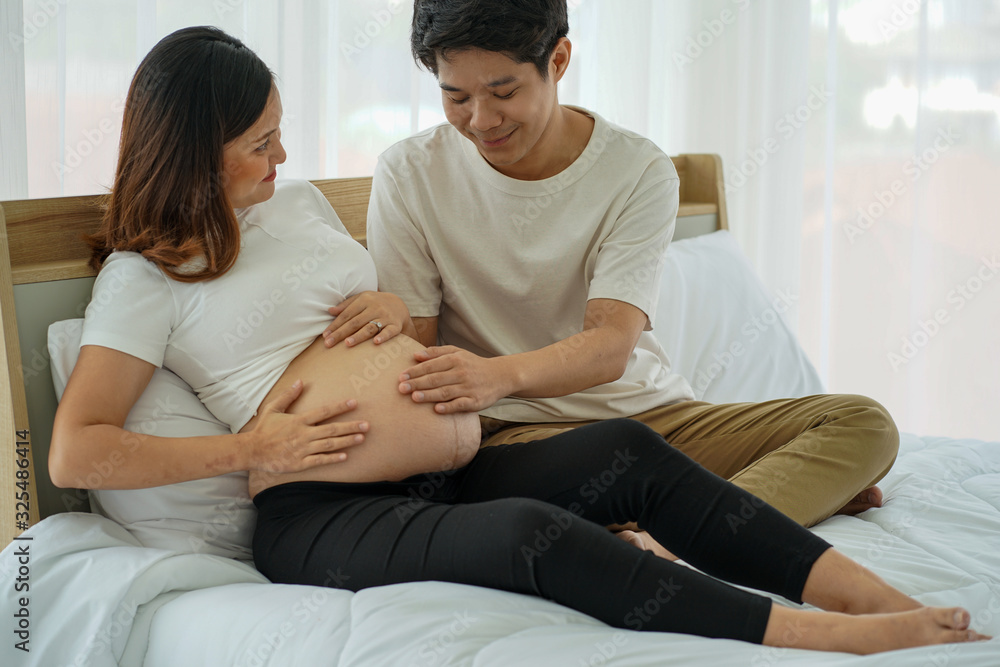 the Asian Young pregnancy woman lay on the bed with her husband tenderness touch the bally with hands in the house the Asian Young pregnancy woman lay on the bed with her husband tenderness touch the bally with hands in the house