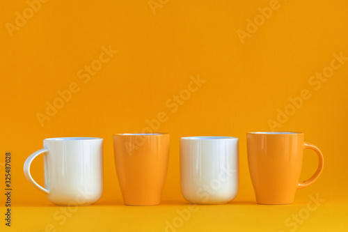 White and yellow coffee cups aligned on yellow background