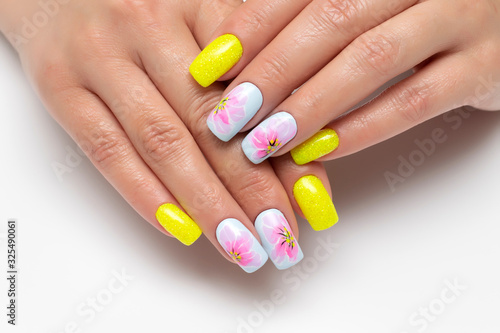 Bright yellow and blue summer manicure with painted flowers on square long nails with sparkles. Sunny manicure. Pink flowers. Close-up on a white background.